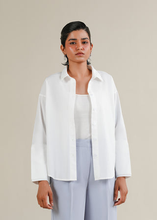 Oversized Button Down Shirt – WS25-188 for Women – Summer Reverie Collection | KOA | Shop Online.
Woman wearing a white shirt and light blue pants against a beige background
