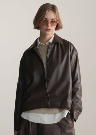 Women wearing a brown leather jacket of KOA over a white shirt and beige sweater on a plain background