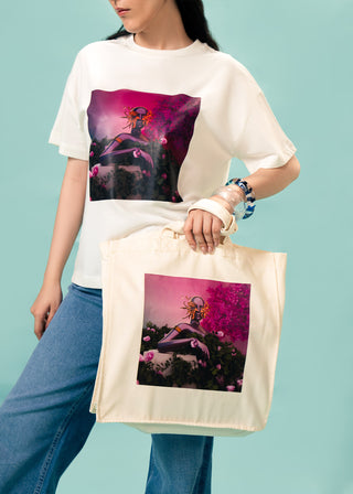 Tote Bag – Eden Reborn by Riza Qureshi – WS25-239 for Women – Art Board 01 Collection | KOA | Shop Online.
Person wearing a white t-shirt and holding a tote bag with a colorful design on a light blue background