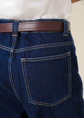 Close-up of blue jeans with a brown belt and white shirt.