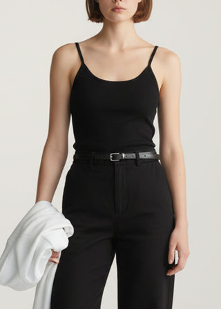 Woman wearing a black 'KOA' tank top and black pants holding a white garment against a neutral background