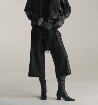 Women wearing a black leather coat with fringe, black gloves, and black KOA leather Pants on a plain background
